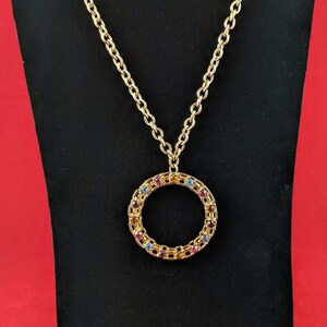 May include: A gold chain necklace with a round pendant. The pendant is made of gold and has a circle design with colorful gemstones.