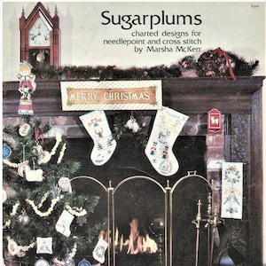 May include: A book cover featuring a Christmas scene with a fireplace, stockings, a decorated tree, and two dolls. The title of the book is "Sugarplums" and the text "charted designs for needlepoint and cross stitch by Marsha McKerr" is also visible.