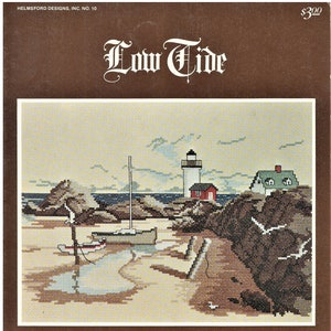 May include: A cross-stitch pattern featuring a lighthouse, a small house, and two boats on a sandy beach. The pattern is titled "Low Tide" and is by Susan Stafford Helming. The pattern is from Helmsford Designs, Inc. No. 10.