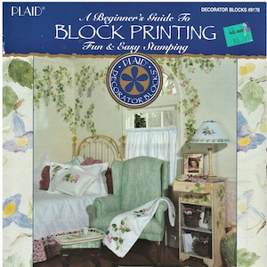 May include: A book cover with a blue background and the title "A Beginner's Guide To Block Printing Fun & Easy Stamping". The cover features a photo of a living room with a green armchair, a bed, and a side table. The book is designed by Jane Gauss & Liza Glenn.