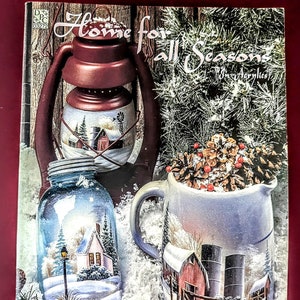 Könnte beinhalten: Ein Buch mit dem Titel "Home for All Seasons in Acrylics" von Debbie Coons. Der Umschlag zeigt eine bemalte Laterne, ein Einmachglas und einen Krug, die jeweils eine Winterszene darstellen.