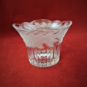 Peut inclure: Un vase en verre transparent avec un motif floral givré. Le vase a un bord festonné et un corps cannelé.