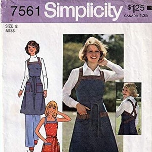 May include: A vintage sewing pattern for a dress with an apron overlay. The pattern is for size 8 and includes instructions on how to sew the garment. The pattern is from Simplicity and has the number 7561 on it.