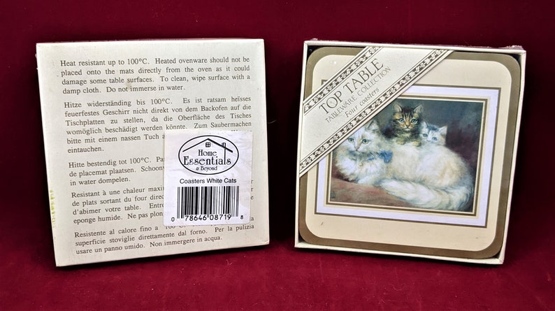 K&ouml;nnte beinhalten: Set mit vier wei&szlig;en Keramik-Untersetzern mit einem Bild von drei wei&szlig;en Katzen. Die Untersetzer sind in einer wei&szlig;en Schachtel verpackt, auf der vorne der Text "Top Table Tableware Collection Four Coasters" steht.
