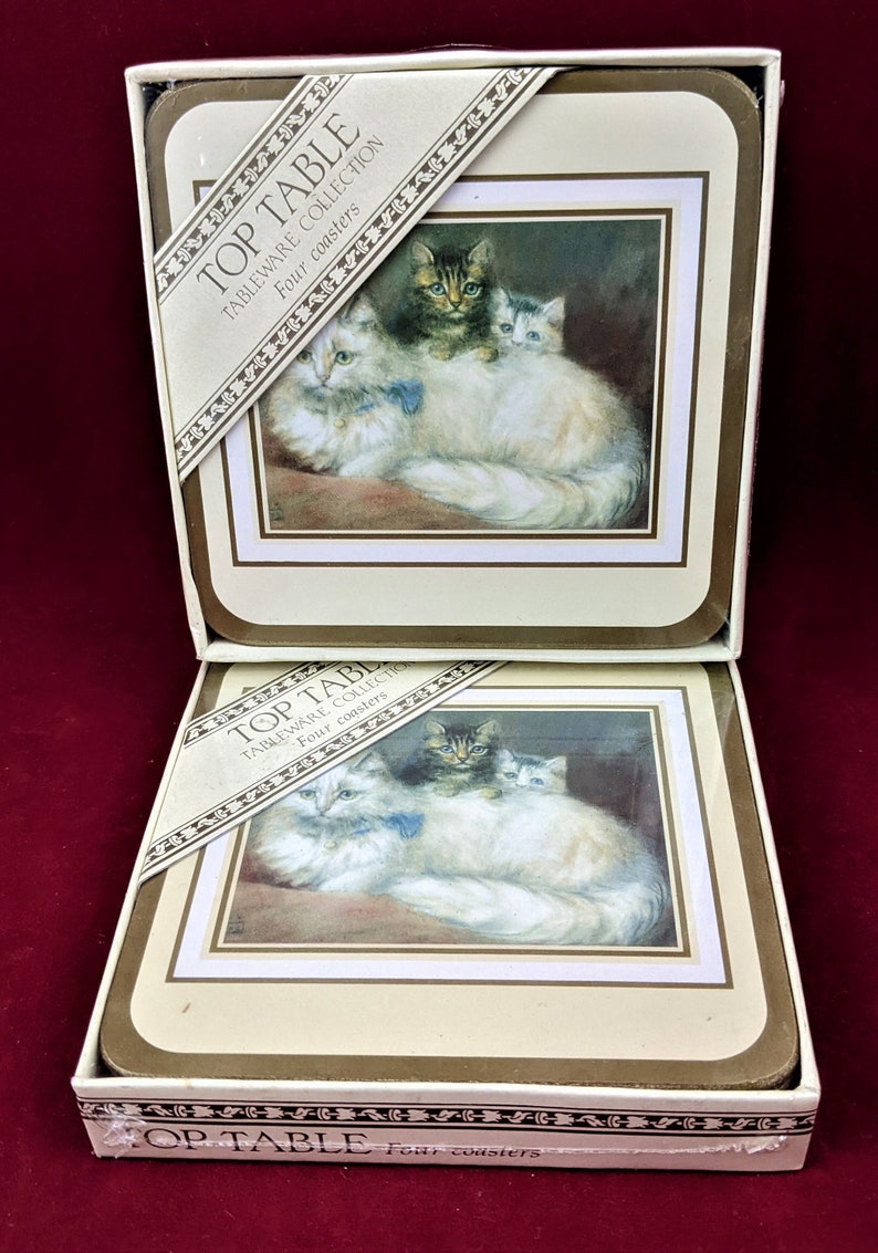 K&ouml;nnte beinhalten: Ein Set mit vier wei&szlig;en Keramik-Untersetzern mit braunem Rand. Die Untersetzer zeigen eine Vintage-Illustration einer wei&szlig;en Katze mit zwei K&auml;tzchen. Die Schachtel tr&auml;gt die Aufschrift "Top Table Tableware Collection Four Coasters".