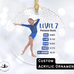May include: A clear acrylic ornament with a photo of a gymnast in a blue leotard. The ornament has gold glitter accents and the text "LEVEL 7 Personal Bests" with scores for various events. The bottom text reads "CUSTOM ACRYLIC ORNAMENT".