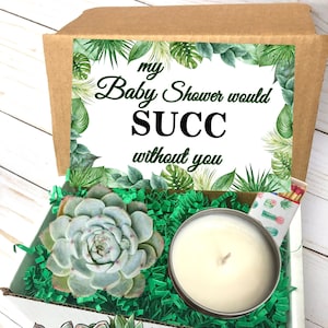 May include: A white gift box with green tissue paper and a succulent plant. The box has a label that says "my Baby Shower would SUCC without you". The box also contains a white candle in a metal tin. The box is labeled "Plants of Paradise - The Plant Gift Shop".
