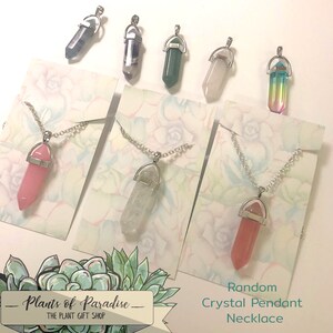 May include: Assorted crystal pendant necklaces on silver chains. The crystals are various colors, including pink, clear, green, and a rainbow gradient. Each pendant is displayed on a card with a floral design. The text "Random Crystal Pendant Necklace" is visible.