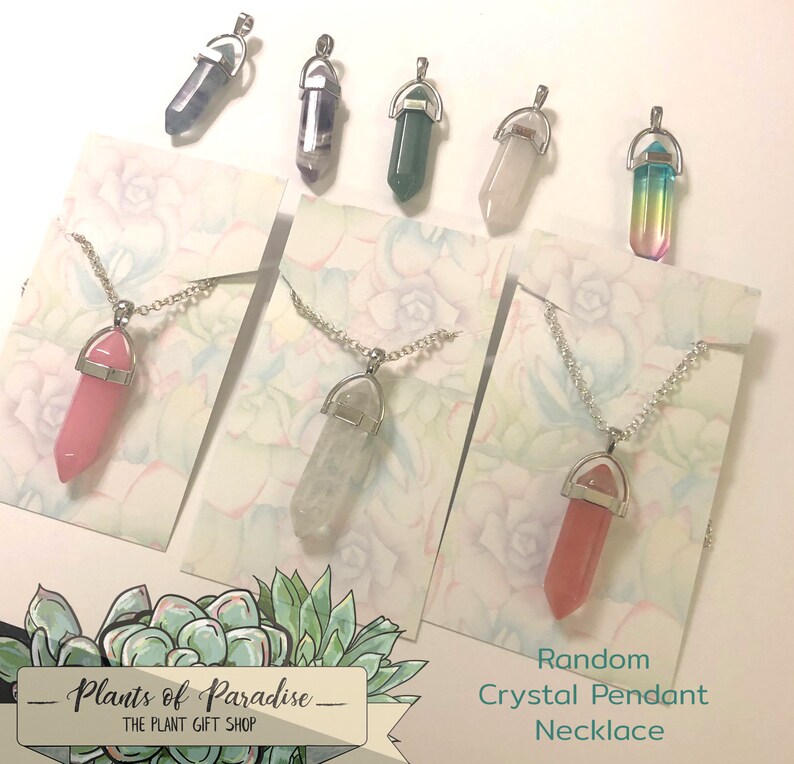 May include: Assorted crystal pendant necklaces on silver chains. The crystals are various colors, including pink, clear, green, and a rainbow gradient. Each pendant is displayed on a card with a floral design. The text "Random Crystal Pendant Necklace" is visible.