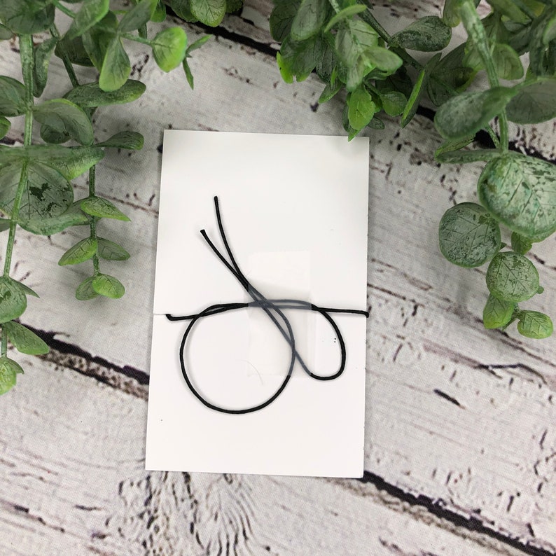 May include: A white card with a black string tied around it in a knot.