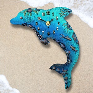 May include: A dolphin-shaped wall clock featuring a gradient of blue and teal colours. The surface is decorated with embossed aquatic elements including seashells, starfish, and fish. Black clock hands point to black numbers from 1 to 12.