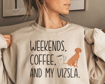 May include: A beige sweatshirt with the text "Weekends, Coffee, and My Vizsla." A cartoon image of a brown Vizsla dog and a coffee cup with a heart on it are also on the sweatshirt.
