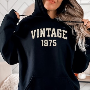 May include: Black hooded sweatshirt with a vintage 1975 design in a cream color.