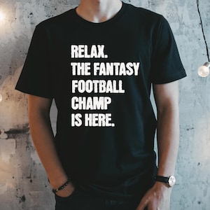Op de afbeelding: Zwart T-shirt met witte tekst die "Relax. The Fantasy Football Champ Is Here." luidt.