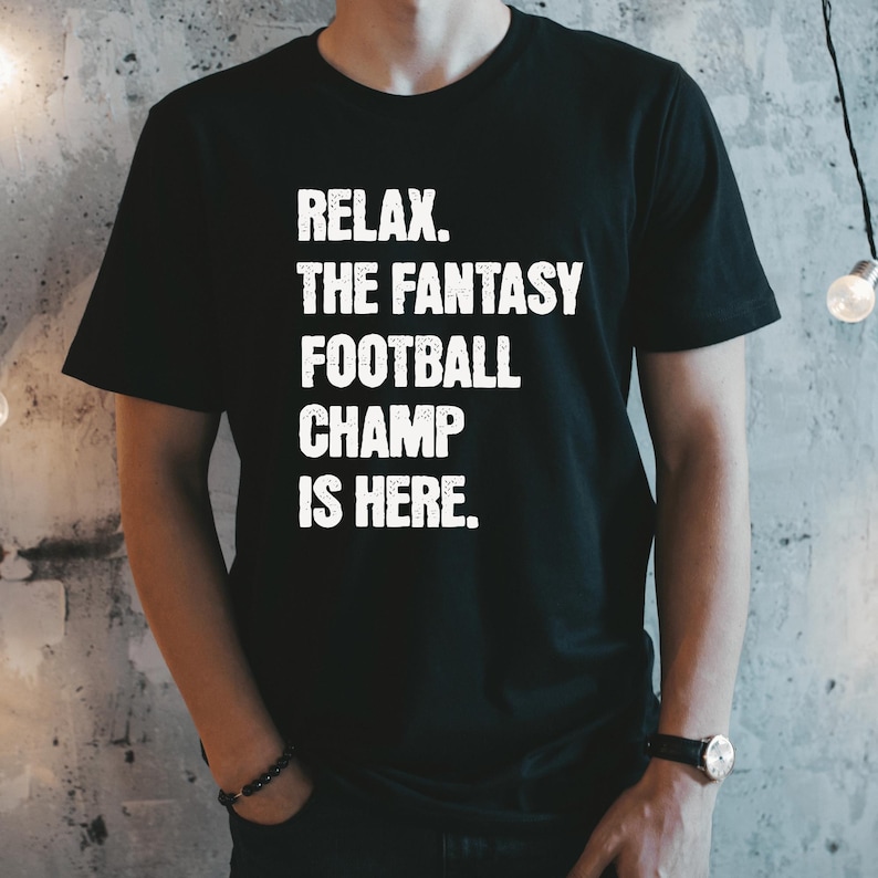 Op de afbeelding: Zwart T-shirt met witte tekst die "Relax. The Fantasy Football Champ Is Here." luidt.