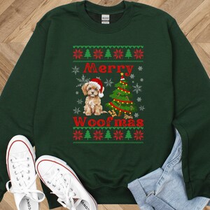 May include: A dark green crewneck sweatshirt featuring a graphic of a puppy wearing a Santa hat next to a decorated Christmas tree. The text Merry Woofmas is printed in red. The design includes snowflake and evergreen tree patterns.