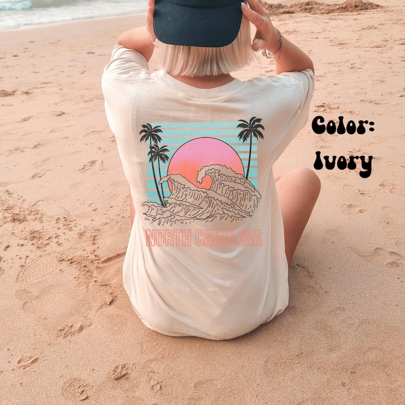 May include: Ivory t-shirt with a graphic of a sunset over waves and palm trees. The text "NORTH CAROLINA" is printed below the graphic.