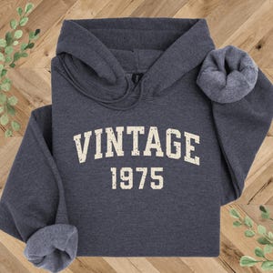 May include: A dark gray hooded sweatshirt with the text "Vintage 1975" printed in white on the front.