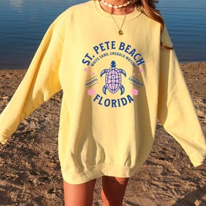 May include: Yellow sweatshirt with a graphic print of a sea turtle and the text "St. Pete Beach White Sand, Emerald Waters Tranquil Currents Florida".