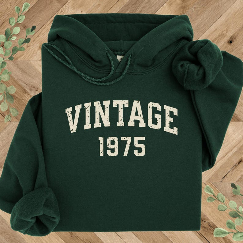 May include: A dark green hooded sweatshirt with the text "Vintage 1975" in a cream color.