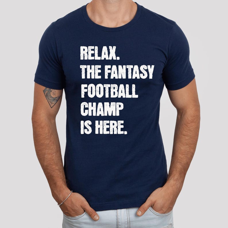 Op de afbeelding: Een donkerblauw t-shirt met witte tekst die "Relax. The Fantasy Football Champ Is Here." luidt.