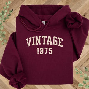 May include: Burgundy hooded sweatshirt with the text "Vintage 1975" in white.