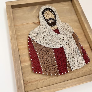 Könnte beinhalten: Ein gerahmtes String-Art-Bild, das eine Person mit Bart und langem Haar darstellt, die eine weiße Robe trägt. Die String Art ist mit rotem, weißem und braunem Garn gefertigt.