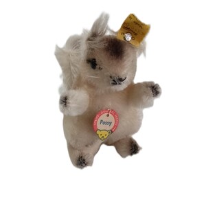 Könnte beinhalten: Ein Vintage-Plüschkaninchen mit cremefarbenem Körper, braunen Akzenten und einem "Possy"-Etikett. Das Spielzeug hat ein gelbes Etikett am Ohr. Das Kaninchen steht aufrecht mit ausgestreckten Armen.