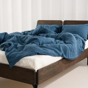 May include: A bed with a dark wood frame and black legs. The bed is covered with a blue comforter and pillows. The sheets are white. The background is a white wall with vertical stripes.