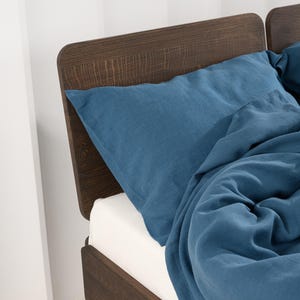 May include: A bed with a dark brown wooden headboard and a white mattress. The bed is covered with blue bedding, including a pillow and a duvet. The headboard has a textured wood grain appearance.