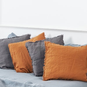 May include: A set of five decorative throw pillows with a frayed edge. The pillows are in shades of gray and orange.