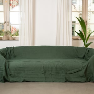 May include: A dark green linen sofa throw draped over a couch in a modern living room. The throw is made of a soft, natural fabric and has a relaxed, casual look.