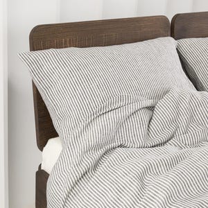 Könnte beinhalten: Ein Bett mit einem dunkelbraunen Holzkopfteil und Bettwäsche mit einem vertikalen Nadelstreifenmuster in Weiß und Anthrazit. Das Set besteht aus einem Kissen und einem Bettbezug, die beide das gleiche durchgehende Streifenmuster zeigen.