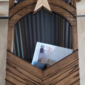 May include: Wooden flag display case with a dark brown finish. The top section features a blue fabric with white stars, and a wooden arrow. The case has a glass front and a document inside.
