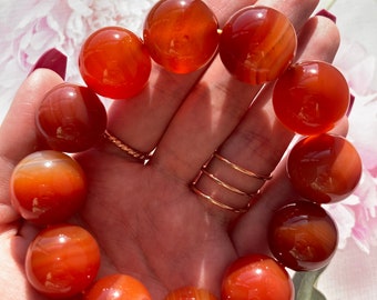 May include: A bracelet made of carnelian beads. The beads are a deep orange color and have a smooth, polished finish. The bracelet is strung on a clear elastic cord.