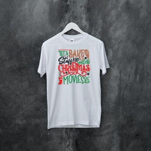 Pu&ograve; includere: Maglietta bianca con una grafica verde e rossa che dice "Let's Bake Stuff and Watch Christmas Movies".