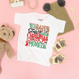 Pu&ograve; includere: Maglietta bianca con una grafica rossa, verde e marrone che dice "Let's Baked Stuff and Watch Christmas Movies".