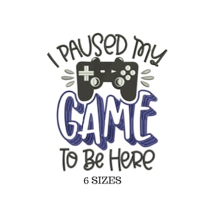 Może przedstawiać: Haftowany wzór przedstawiający kontroler do gier wideo z tekstem "Zatrzymałem grę, żeby tu być" w kolorze niebieskim i czarnym. Zawiera również tekst "6 ROZMIARÓW".