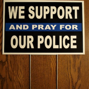 May include: A black and white sign with blue text that reads "We Support and Pray for Our Police".