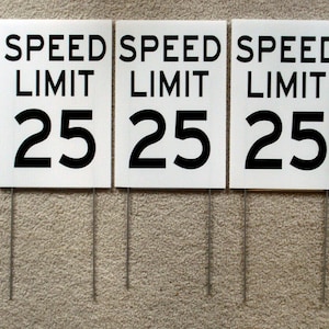Op de afbeelding: Vijf witte snelheidsbegrenzingsborden met zwarte tekst. Elk bord toont "SPEED LIMIT 25".