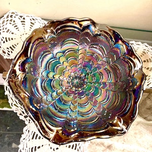 May include: Iridescent glass bowl with a floral design. The bowl features a spectrum of colors, including blues, greens, purples, and golds. The rim has a scalloped edge. The bowl is likely vintage or antique.