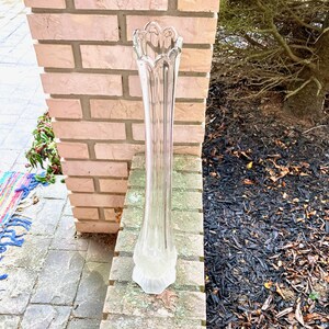 Op de afbeelding: Een heldere glazen vaas met een geribbeld ontwerp. De vaas is hoog en slank, met een uitlopende opening aan de bovenkant.