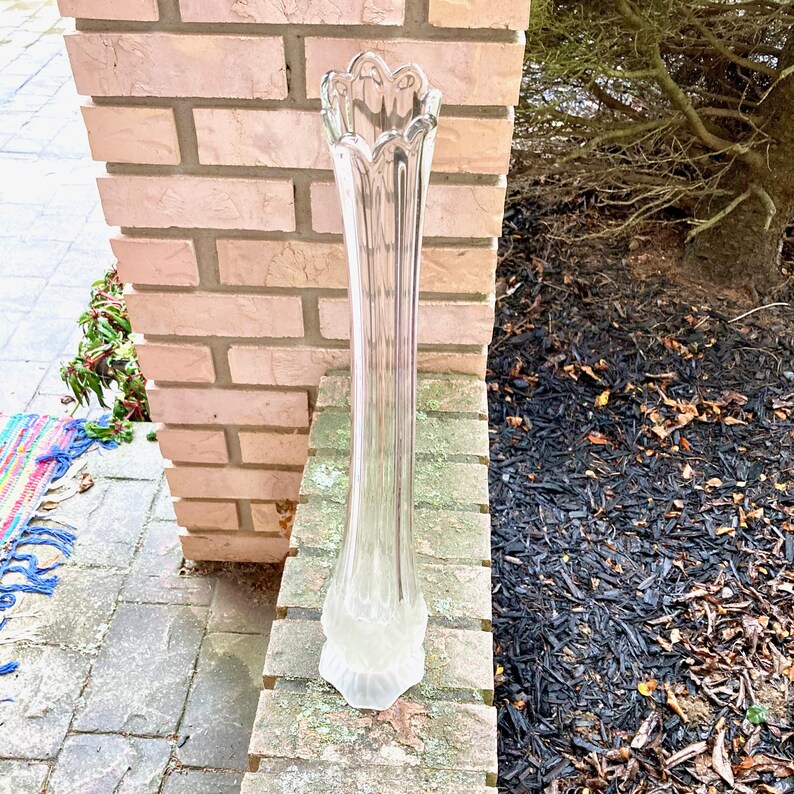 Op de afbeelding: Een heldere glazen vaas met een geribbeld ontwerp. De vaas is hoog en slank, met een uitlopende opening aan de bovenkant.