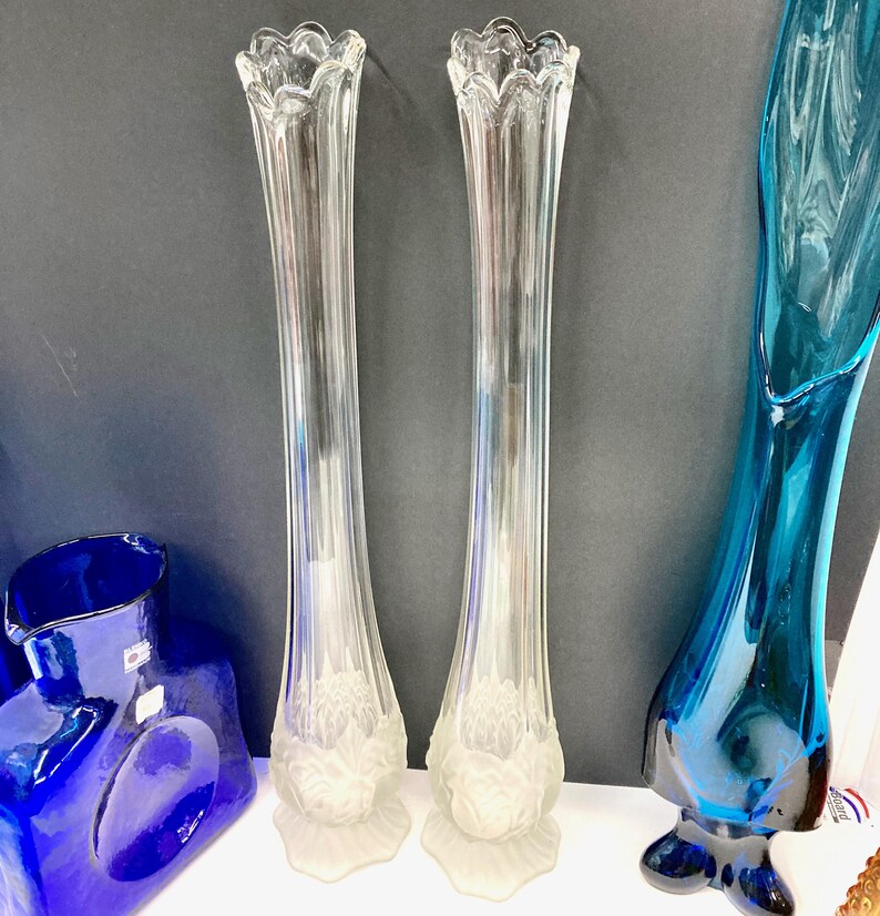 Op de afbeelding: Twee heldere glazen bloemenvazen met een getextureerd, mat ontwerp aan de basis. De vazen zijn hoog en slank met een gegolfde rand.
