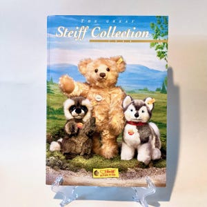 May include: A book titled "The Great Steiff Collection 2000" featuring a brown teddy bear, a raccoon, and a husky dog. The book has a yellow and white Steiff button in ear logo on the bottom.