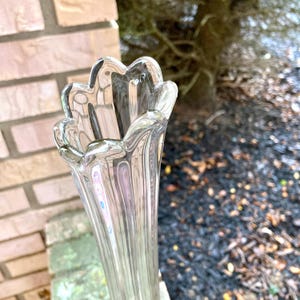 Op de afbeelding: Een heldere glazen vaas met een geribbeld ontwerp en een gegolfde rand. De vaas is hoog en slank, met een smalle opening.