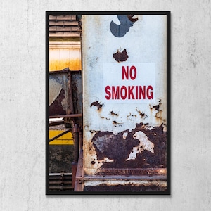 May include: A framed wall art print featuring a weathered, rusted metal surface with peeling white paint and a rectangular sign that reads NO SMOKING in bold red letters. The industrial texture shows significant oxidation and decay.