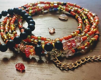 May include: A multi-strand beaded necklace with black, orange, and gold beads. The necklace has a gold chain clasp and is adorned with small, clear crystals.