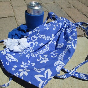 May include: A blue drawstring bag with a white floral pattern. The bag is lying on a brick surface with a blue can cooler and two white and blue hair scrunchies.