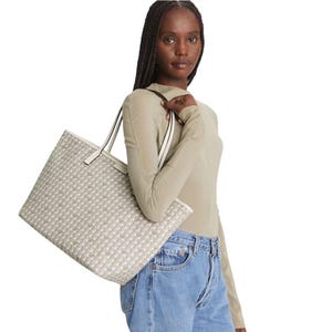 May include: A beige tote bag with a repeating pattern of small white dots. The bag has white handles and trim. The bag is being held by a person wearing a light green long-sleeved top and blue jeans.